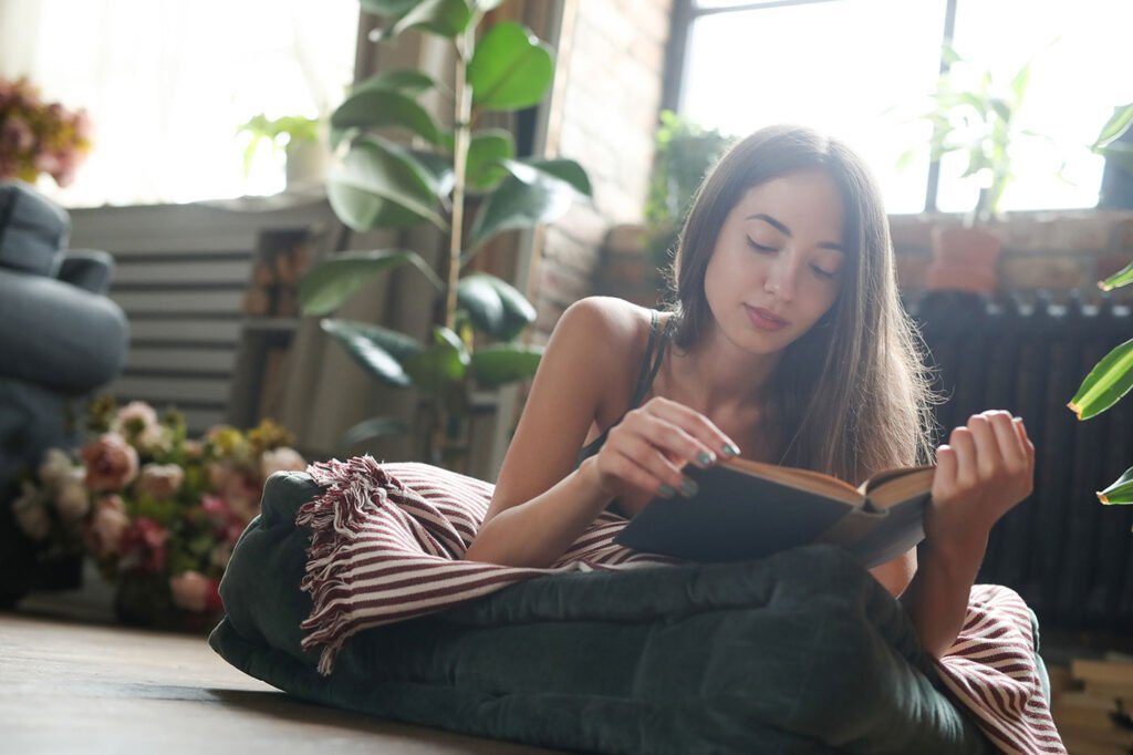 una mujer leyendo un libro de espiritualidad relajada en su cojín con libros y mandalas